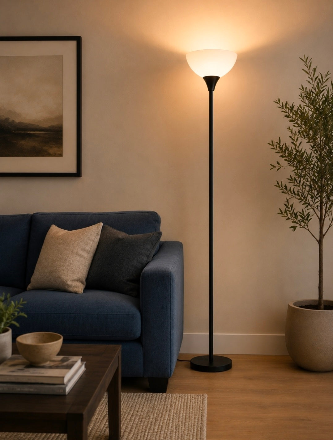 A minimalist black floor uplighter lamp illuminating a cozy living room corner next to a blue sofa.