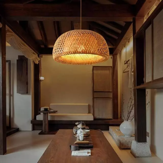 ​A large dome-shaped pendant light made of woven bamboo hanging over a wooden table in a traditional room.