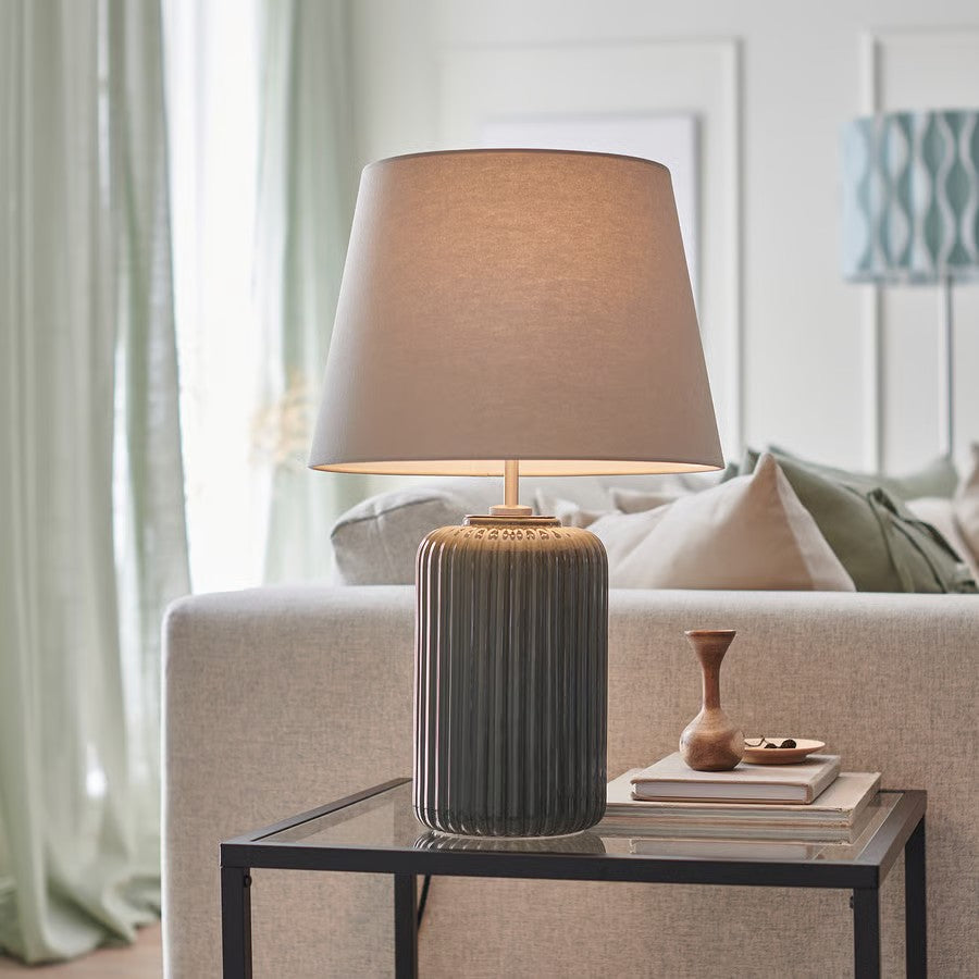 Grey fabric table lamp with a ribbed ceramic base resting on a glass top table.