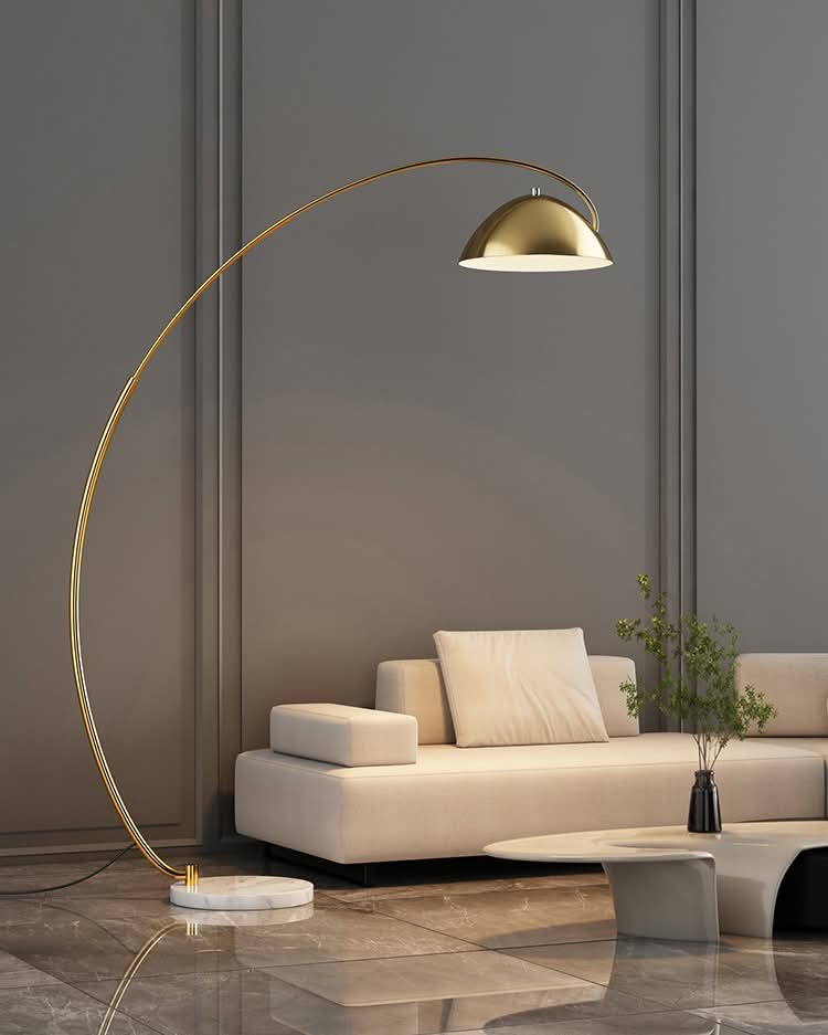 A gold arc floor lamp with a marble base and integrated small circular table standing over a white sofa in a gray room.