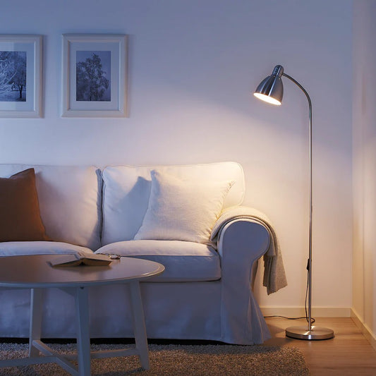 A silver metal floor lamp with an adjustable curved neck shining warm light onto a white sofa