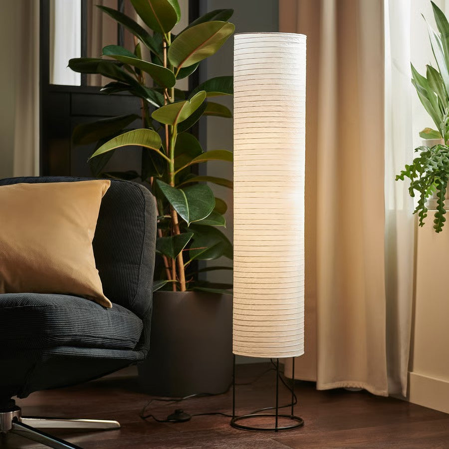 A tall floor lamp with a black metal base standing next to a green plant and a armchair.