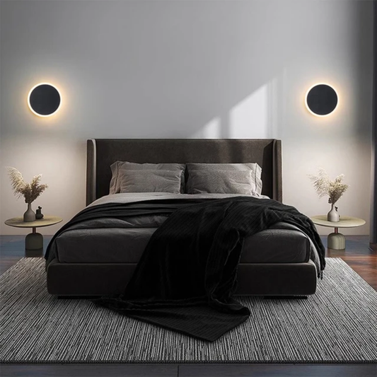 circular black cordless wall lamps emitting a warm glow behind a dark bed