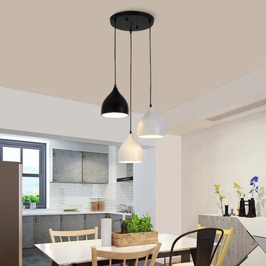Three modern pendant lights hanging from a ceiling in a bright dining and kitchen area. The lights have black and white dome-shaped shades and are suspended by thin black cords from a round black ceiling mount.