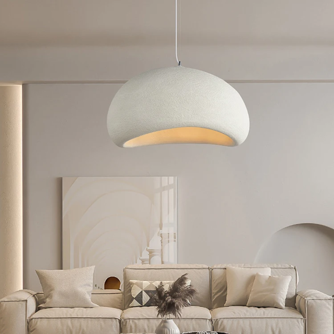 A white textured Wabi Sabi sculptural pendant light hanging above a sofa in a minimalist living room.