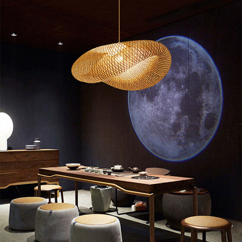 A large, wavy handwoven bamboo pendant light hanging over a wooden table in a dimly lit room.