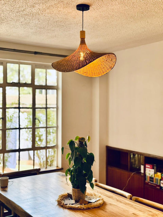 Handwoven straw hat shaped bamboo pendant light hanging over a dining table